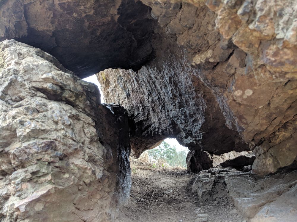 An up close shot of some boulders roughly the size of a compact car, balanced in a position that allows the viewer to see through to the trees on the other side