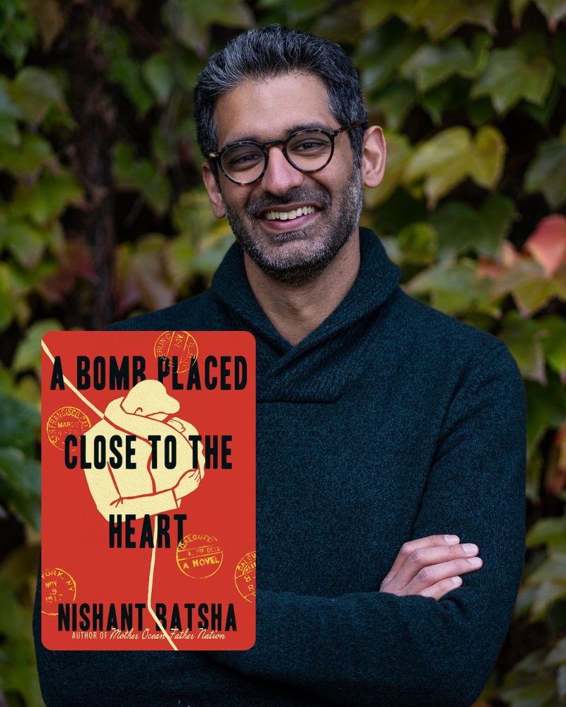 Headshot of writer Nishant Batsha smiling in front of foliage. He is wearing circular glasses and a navy blue long sleeve with his arms crossed in front of him. the cover of new book, A BOMB PLACED CLOSE TO THE HEART, has a red background with a cream graphic of a man and woman in an embrace.