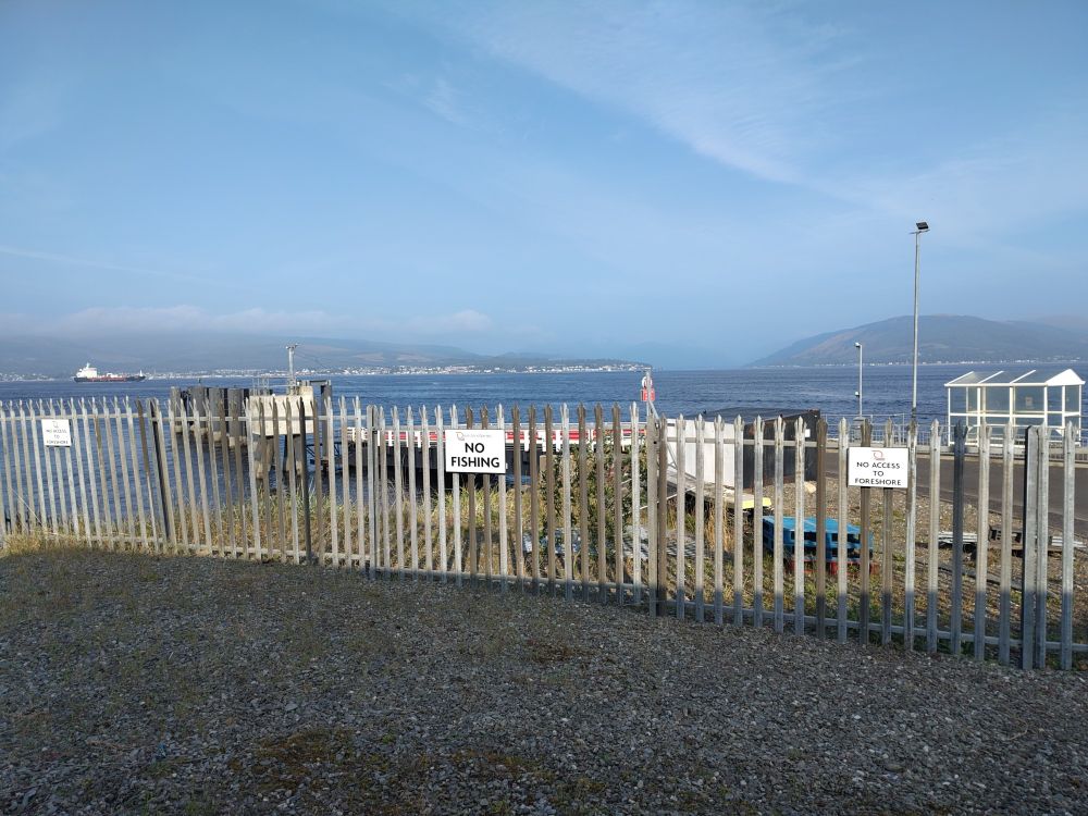 Ferry terminal at the Clyde, with a metal fence between the water and car park. One sign says NO FISHING, two say NO ACCESS TO FORESHORE