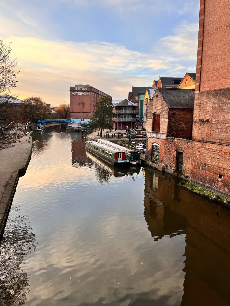 A canal with old buildings, snow covered canal boats and some ducks 