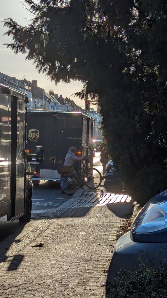 Ältere Dame musste wegen Blockiertem Radweg und Fußweg vom Rad absteigen und auf die Straße ausweichen. Auf der Straße stehen auch noch 2 UPS Paketbullis.