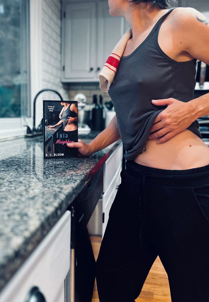 Blake recreating the cover of My Futa Neighbor by K.C. Bloom while holding a paperback of it