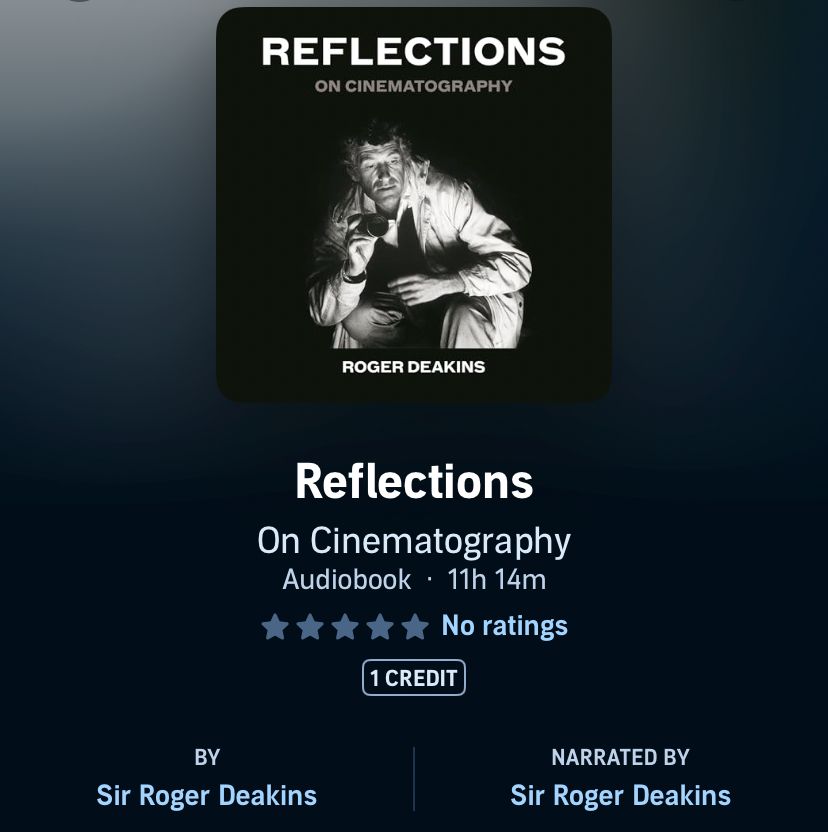 Roger Deakins audio book ‘reflections on cinematography’. Black and white image of him, crouched down holding what looks like a dir viewfinder. 