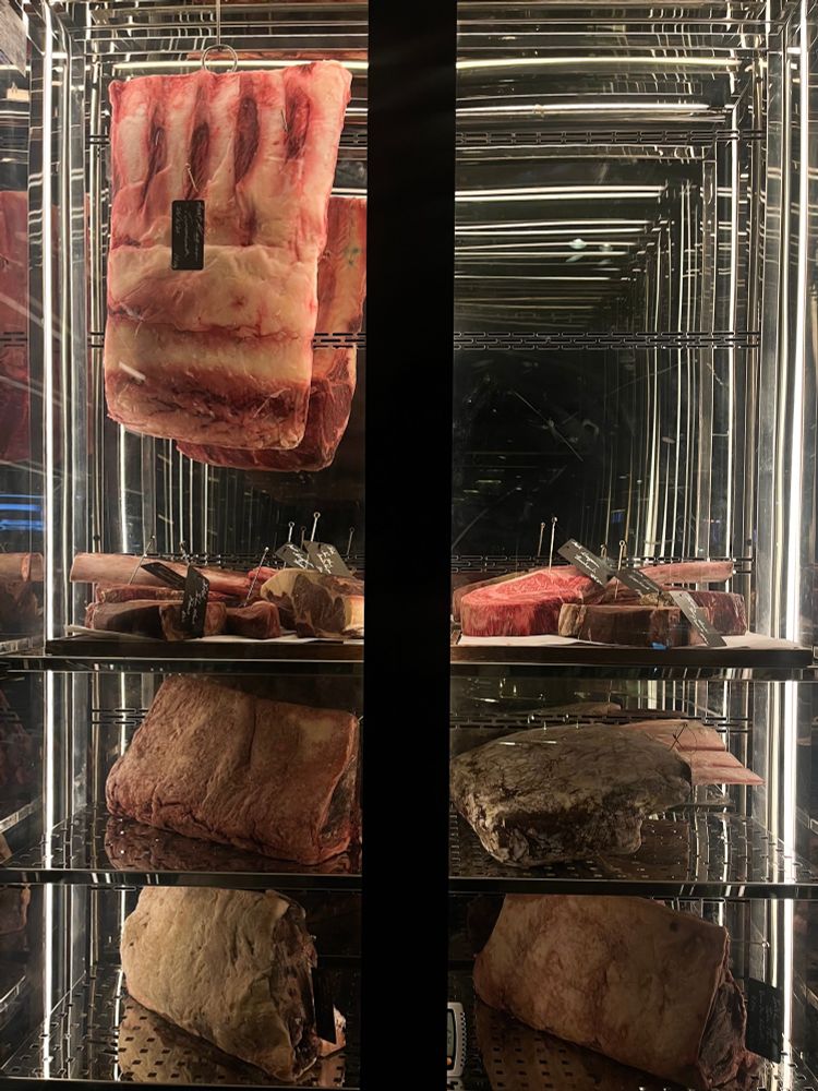A meat cabinet with glass panels holds a variety of steak cuts to be devoured