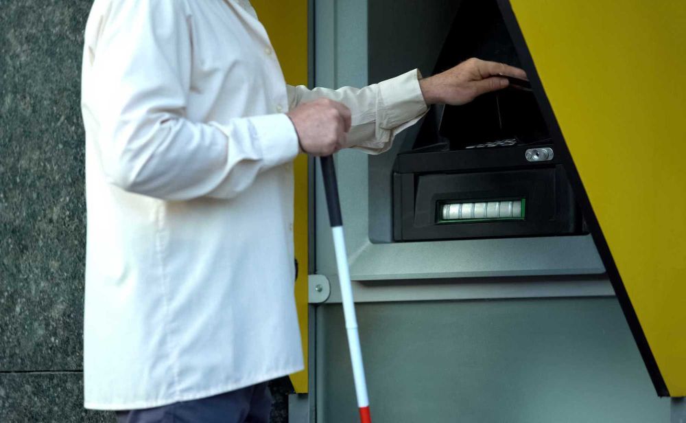 Photo d'illustration montrant un homme en train de retirer de l'argent d'un guichet équipé d'indicateurs tactiles. Photo : iStock / Getty Images / Motortion