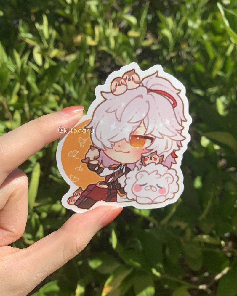 Photo of a matte vinyl sticker featuring Jing Yuan from Hoyoverse's gacha game, Honkai: Star Rail. He's lounging against his sleeping white lion and calmly smiling as little birds perch on his outstretched hand and all over his head.