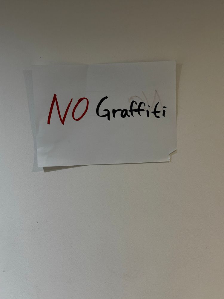 A crude paper sign in the men’s room that reads “No graffiti”