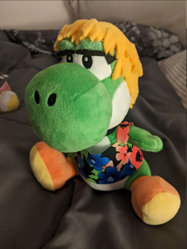 Photo of a plush Yoshi custom-made to resemble Djynn, complete with blond hair, thick eyelashes, and a cute flowery shirt. Also visible: a black collar. What're we gonna do on the bed? *pomf*