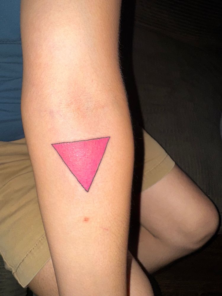 Photo of a forearm with a fresh tattoo; it is a pink triangle with a black outline
