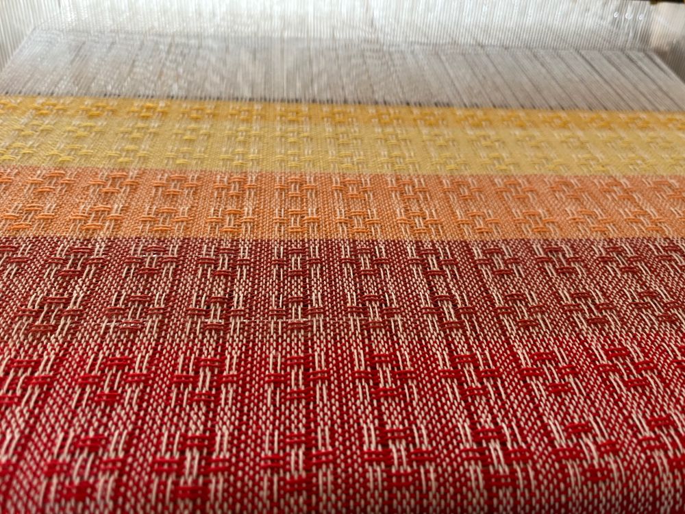 A Huck Warp on the loom with a gradient from red to yellow 