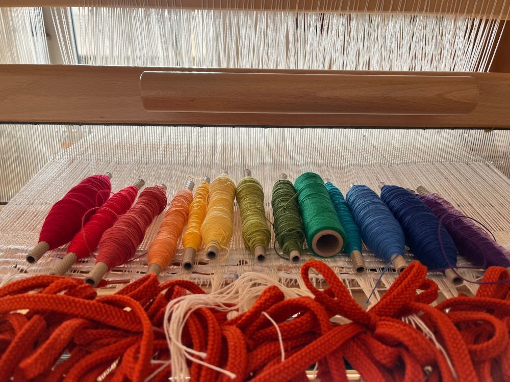 Spools of weft in a rainbow colour order on a recently tied up warp