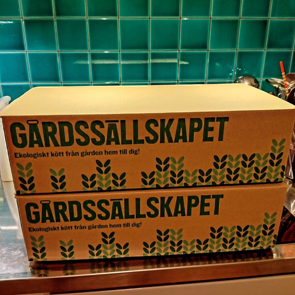 Two cardboard boxes stacked on top of each other, marked with the name of a local meat delivery company.