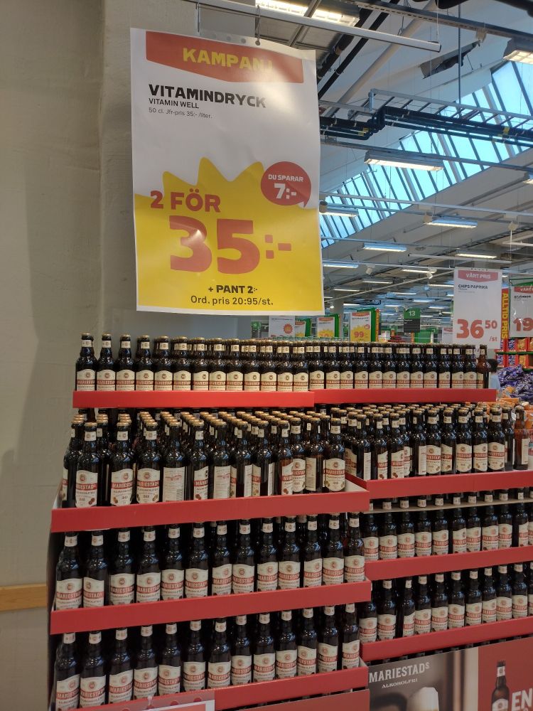 A massive stack of (alcohol free) beers in a supermarket; above the beers, a campaign sign advertises "Vitamin Drink, 2 for 35 kronor".