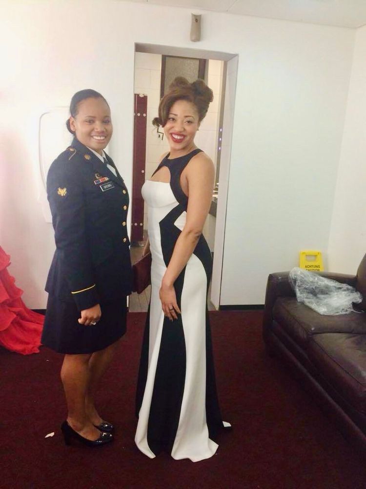 Two women posing,  one in military dress and one in a ball gown before a military ball