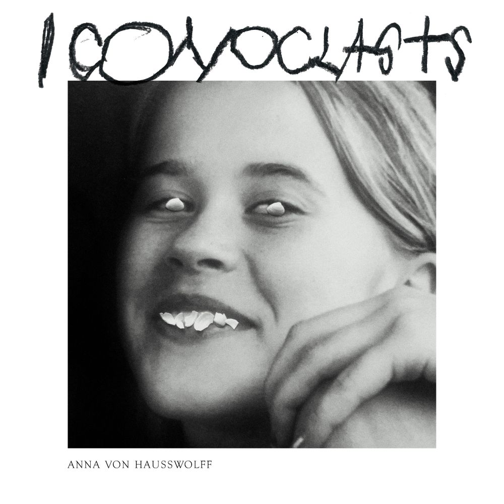 The cover art for ICONOCLASTS. It is a photo of von Hausswolff with a mostly empy border around the photo. In the border across the top is scrawled the album title. Her eyes and teeth are covered over by what looks like seashells and fragments as if it's a photo of a photo with physical objects on top of it.
