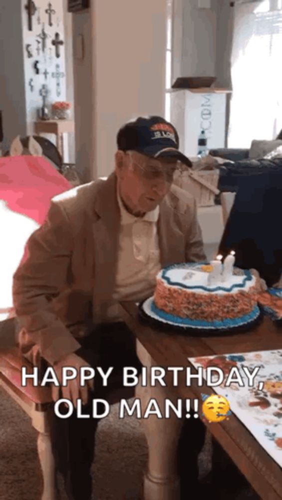 an elderly man is sitting at a table with a cake and candles .