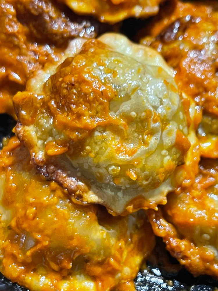 Several round, puffy ravioli that have crisp darker spots, lightly splashed with an orange looking sauce. 