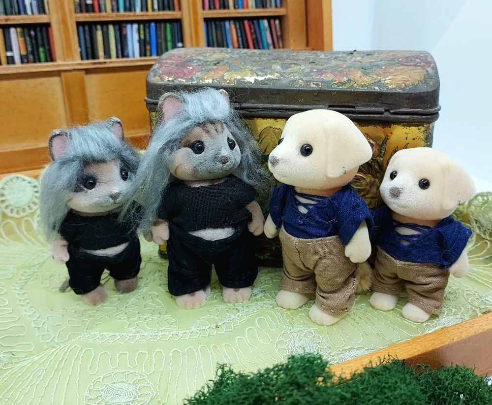 Four Sylvanian Families/Calico Critters Eds and Stedes (one large, one small). Ed is a cat wearing black "leather" pants and a black ter with his tummy out. Stede is a golden retriever wearing brown trousers and a navy shirt with a deep vee and ties. He has one earring.