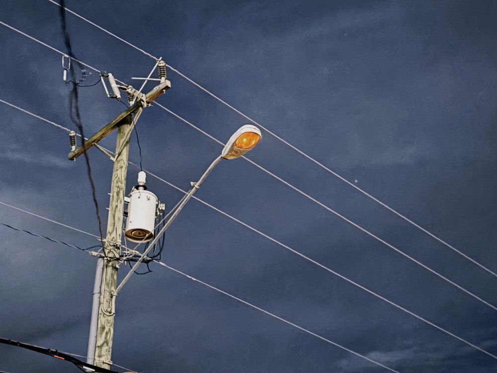 a dim streetlight and power lines across a cloudy night sky.