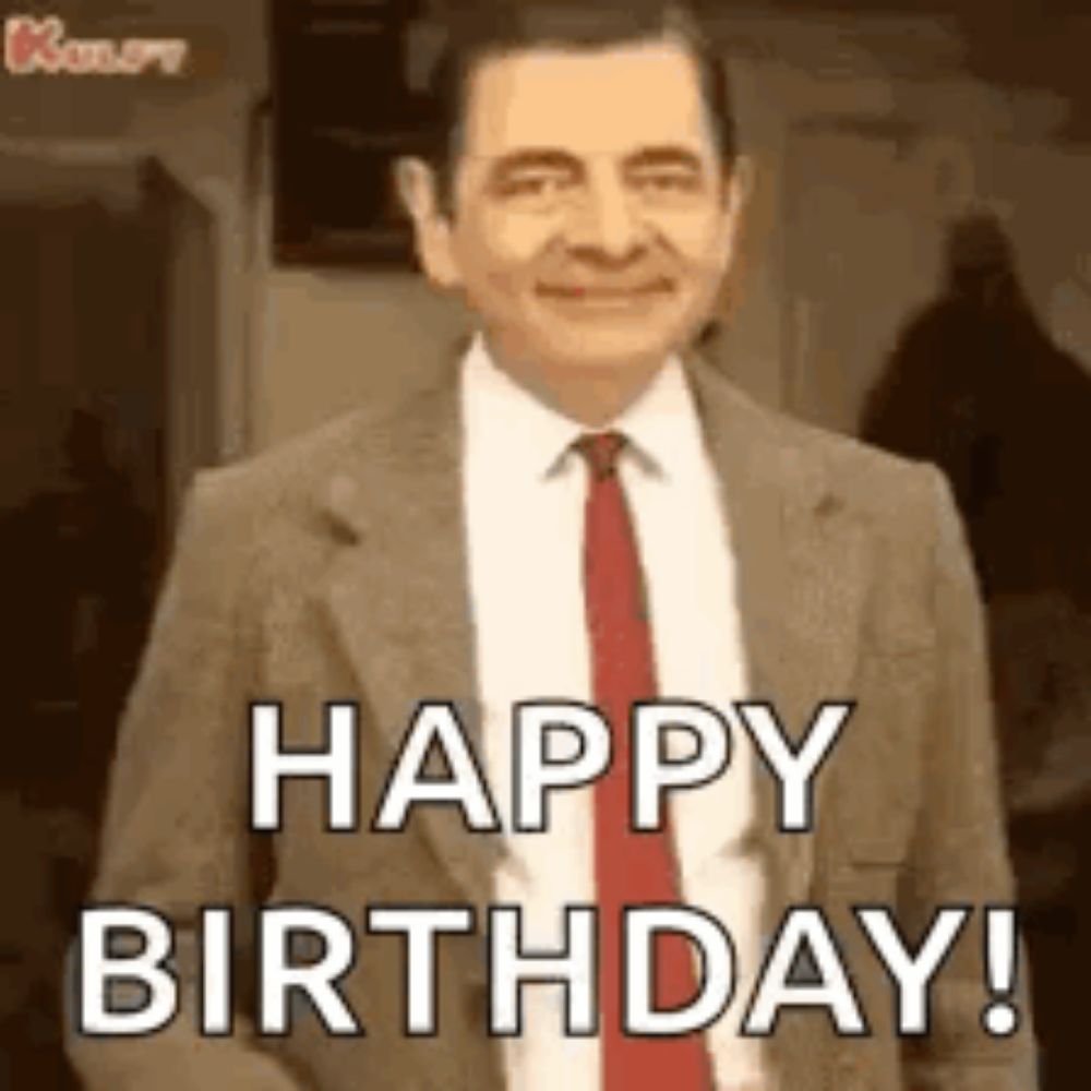 mr bean is wearing a suit and tie and smiling while saying happy birthday .