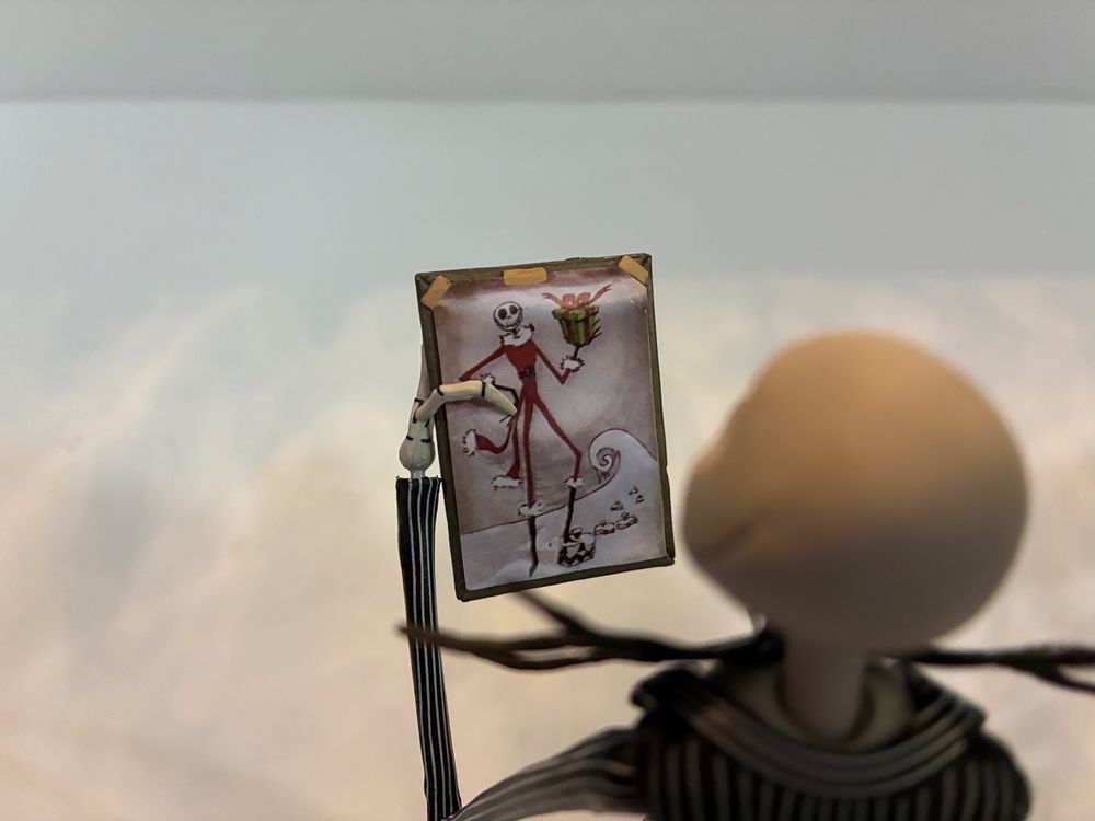 NECA Toys Jack Skellington action figure looking at a picture of the character as Santa Claus.