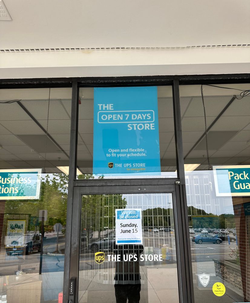 UPS Store Storefront with giant poster that says, “The Open 7 Days Store” with a sign underneath that says, “Closed Sunday June 15”