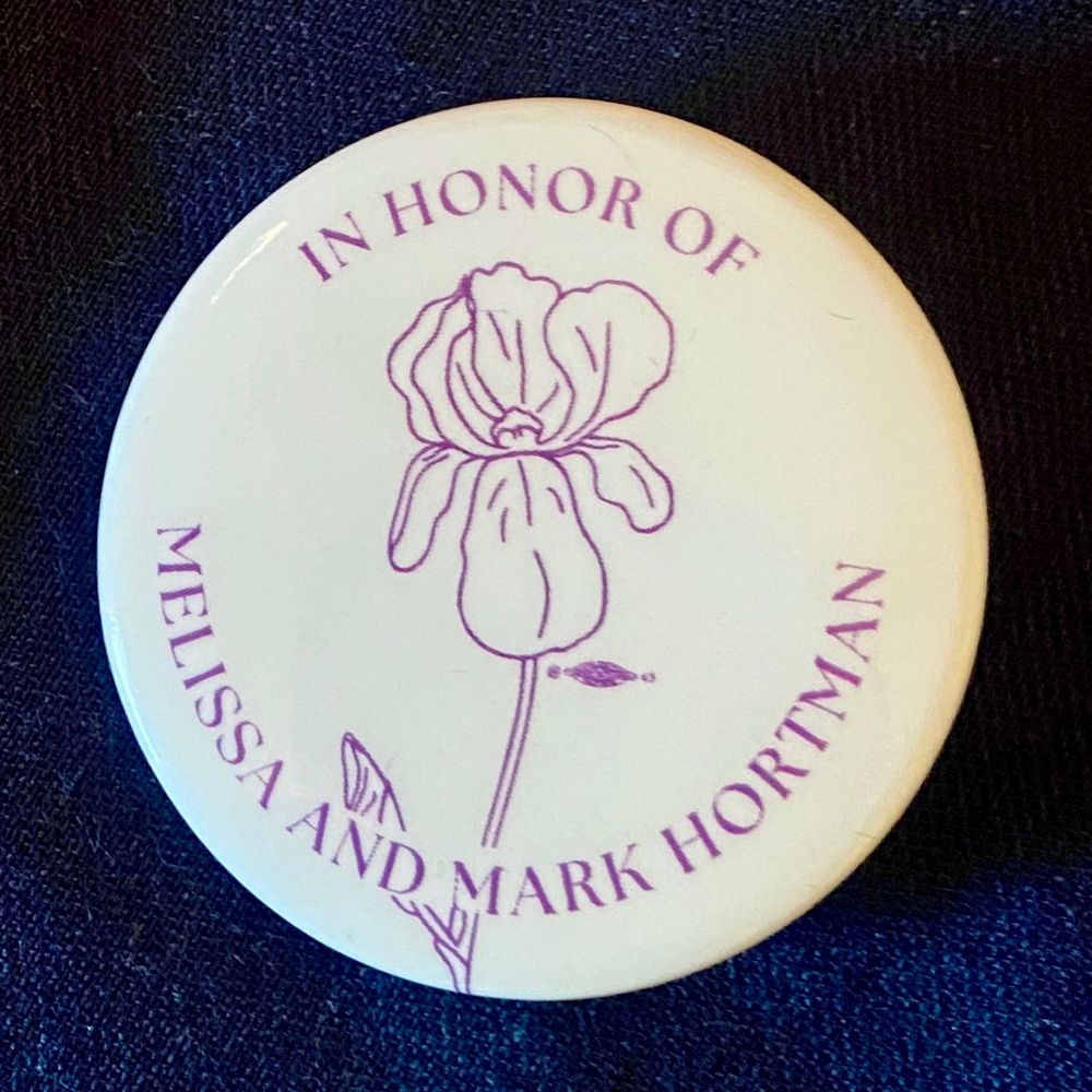Round lapel pin that reads In Honor of Melissa and Mark Hortman with a drawing of an iris bloom in the center.