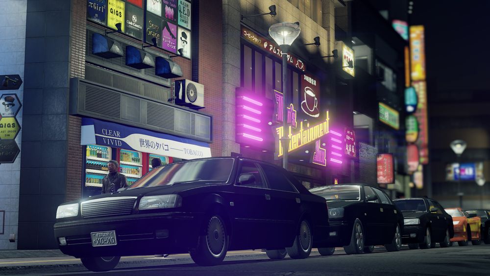 A screenshot from Yakuza: Like A Dragon showing a line of cars parked in front of a neon-soaked row of buildings
