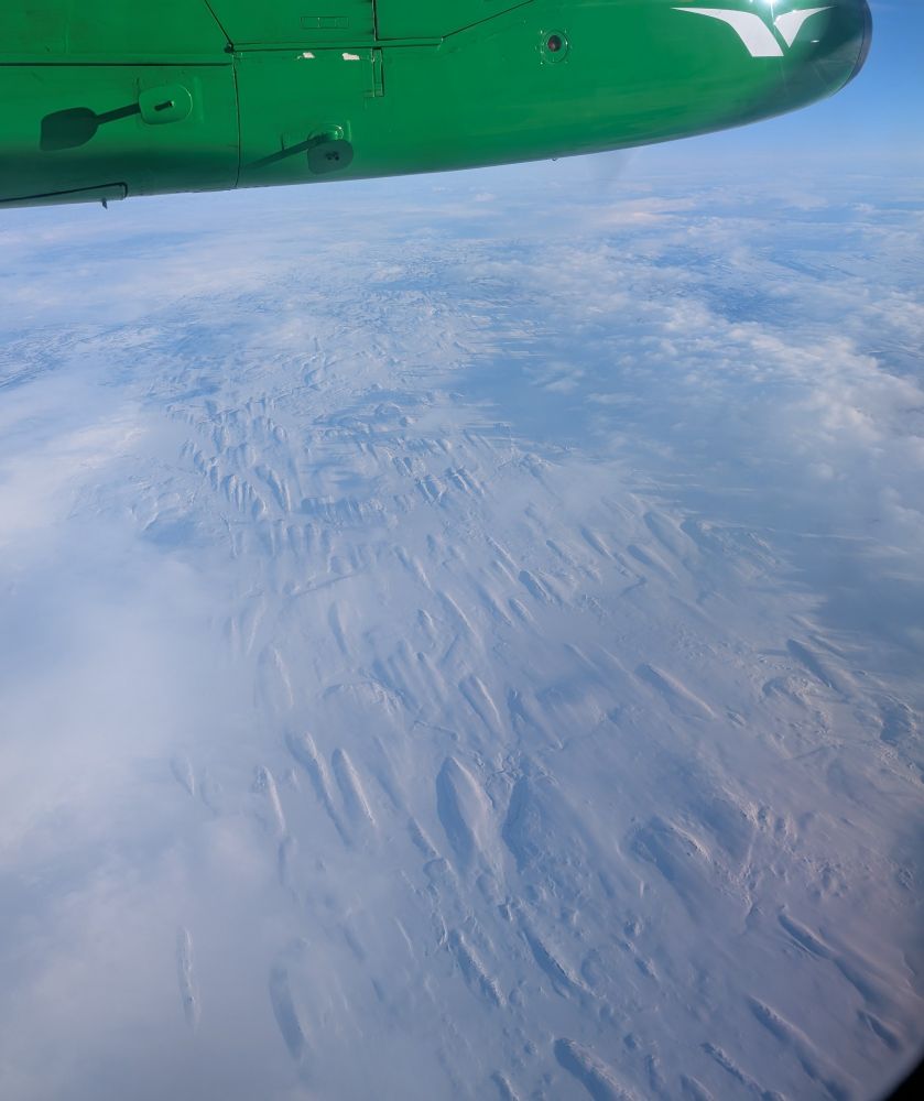 Snow covered landscape as seen from a plane window, showing some streamlined landforms.