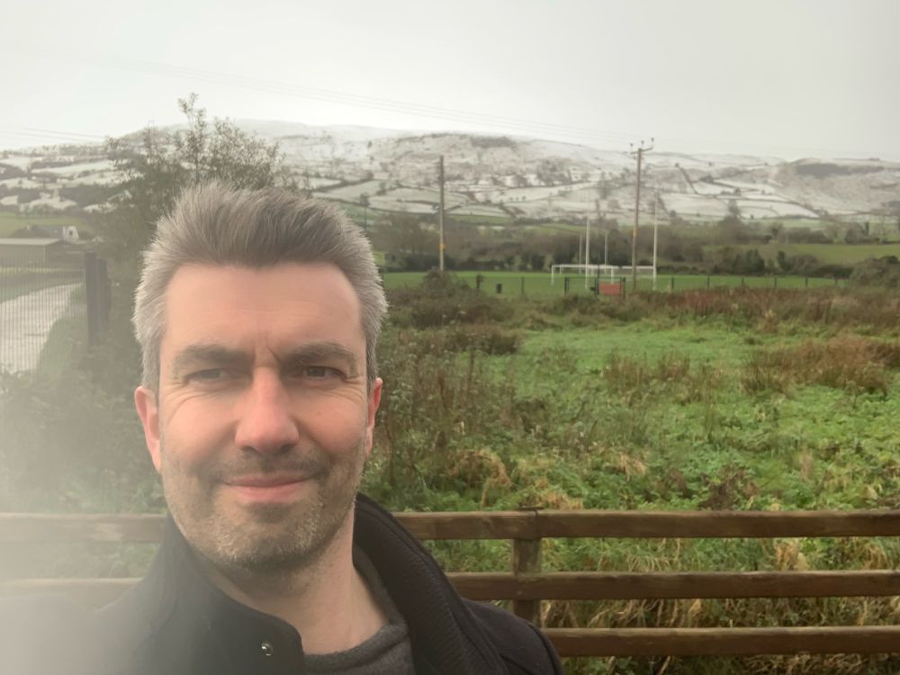 Danny in Carnlough with snowy glens behind him. 
