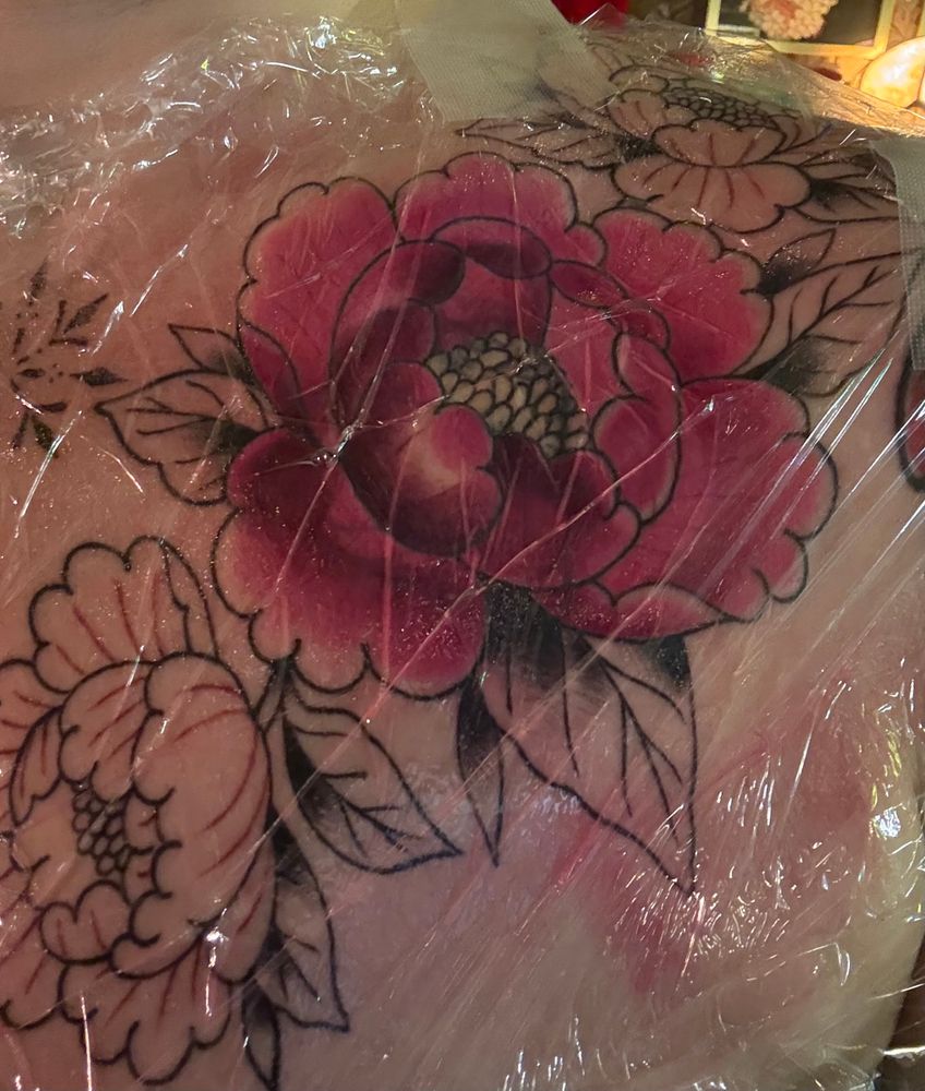 Picture of a chest piece tattoo with flowers lined out. One red flower is filled out