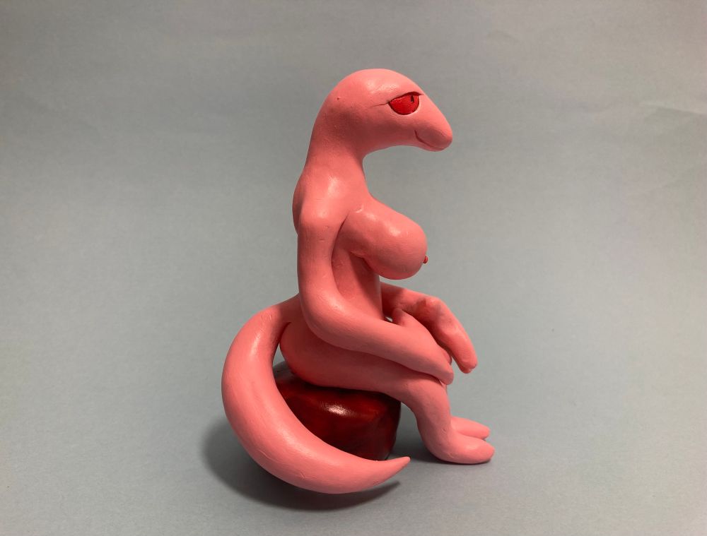 A model of a pink, anthropomorphic snake lady sitting down in the nude, on a blue background. 