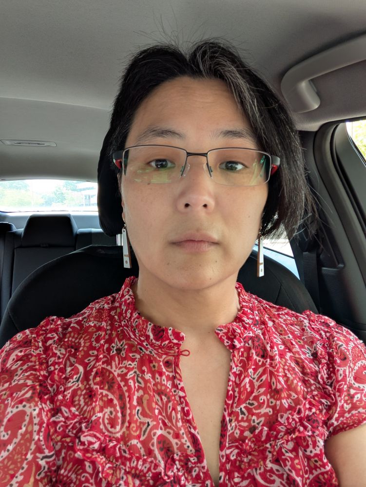 car selfie of me wearing earrings of painted wood depicting a white sperm whale in a stylized geometric fashion