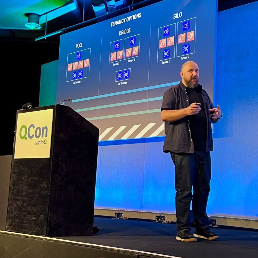 Jon is stood on a conference stage. The slide behind him show three architects relating to multi-tenancy options for SaaS builders 
