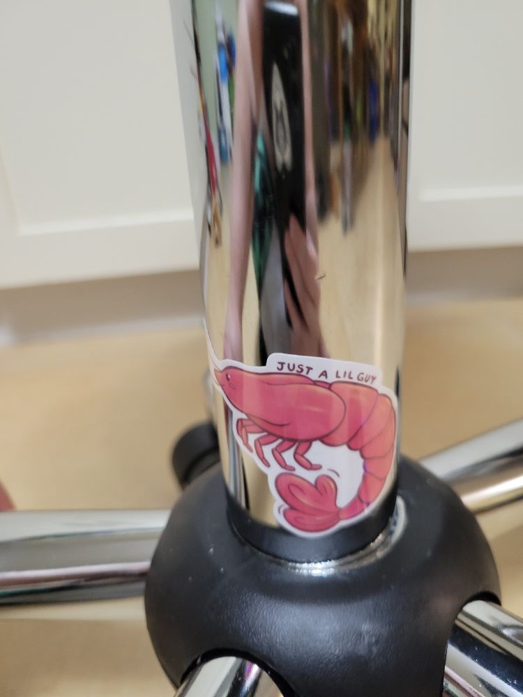 a close up of a sticker of a shrimp on a shiny support post. the sticker of the cartoon shrimp reads 'just a little guy'