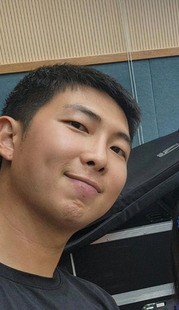 selfie of Namjoon showing a dimple, with a closed smile, shaved hair and a black shirt 