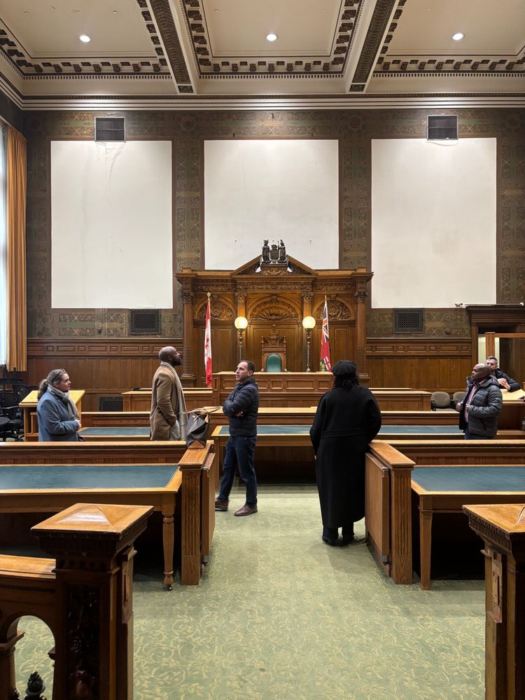 Several people touring a Victorian courtroom featuring decorative woodwork and art nouveau wallpaper
