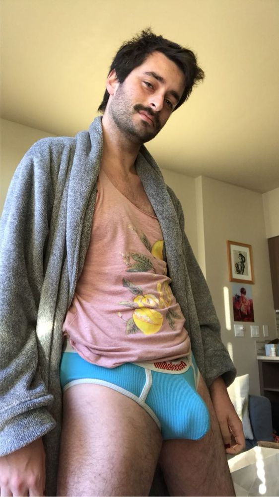 A man in a gray bathrobe, pink tank top, and blue briefs. His bulge is prominent and you can clearly make out balls and shaft 