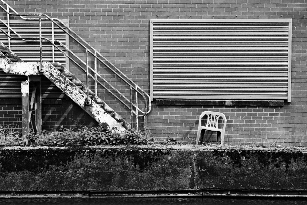 A plastic chair invites a worker in a factory to sit and ponder by the canal