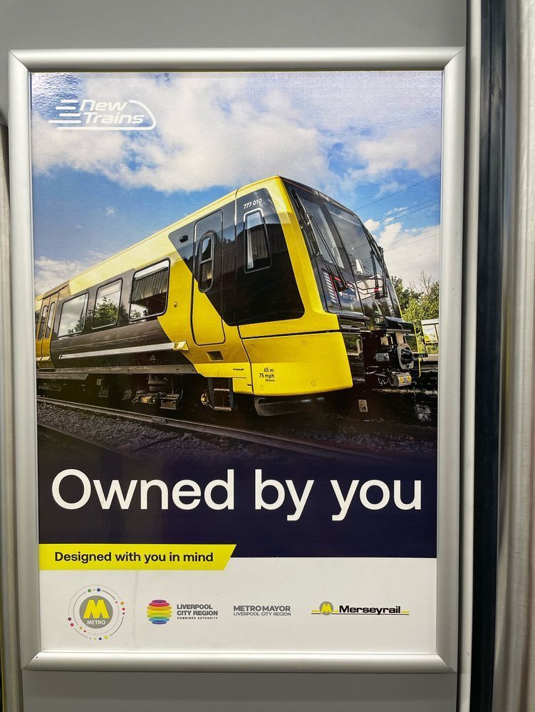 Photo of a poster advertising Merseyrail’s new trains. A large picture of a shiny new class 777 with text underneath “Owned by you. Designed with you in mind”. The logos of Metro, Liverpool City Region CA, Metro Mayor and Merseyrail appear.