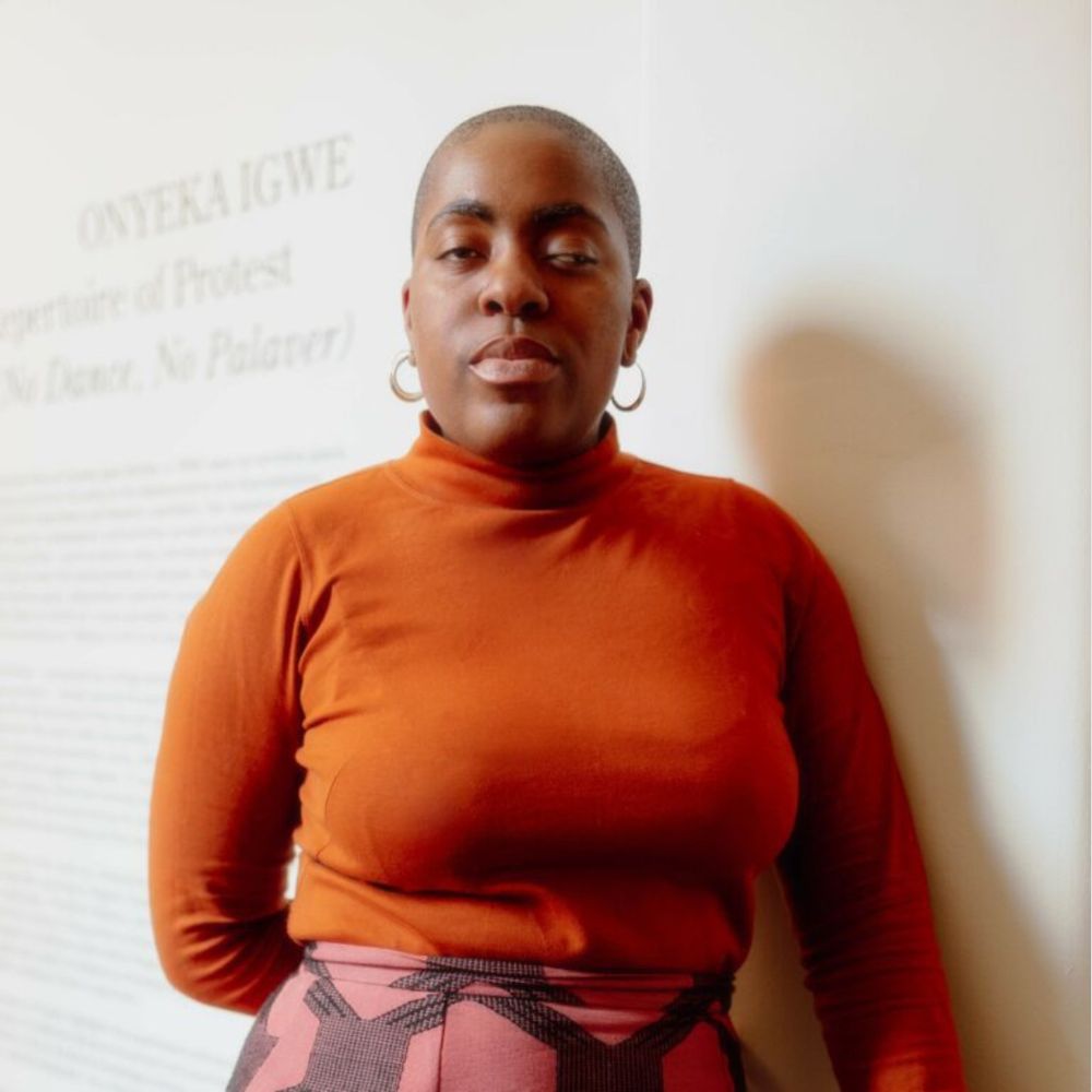 Headshot of the author, Onyeka Igwe, wearing an orange jumper against a white background.