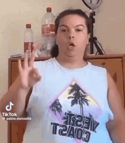 a woman in a tank top is making a peace sign with her hand .