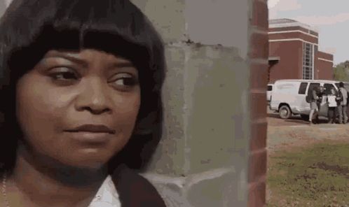 a woman is standing in front of a brick wall with a white van parked in the background