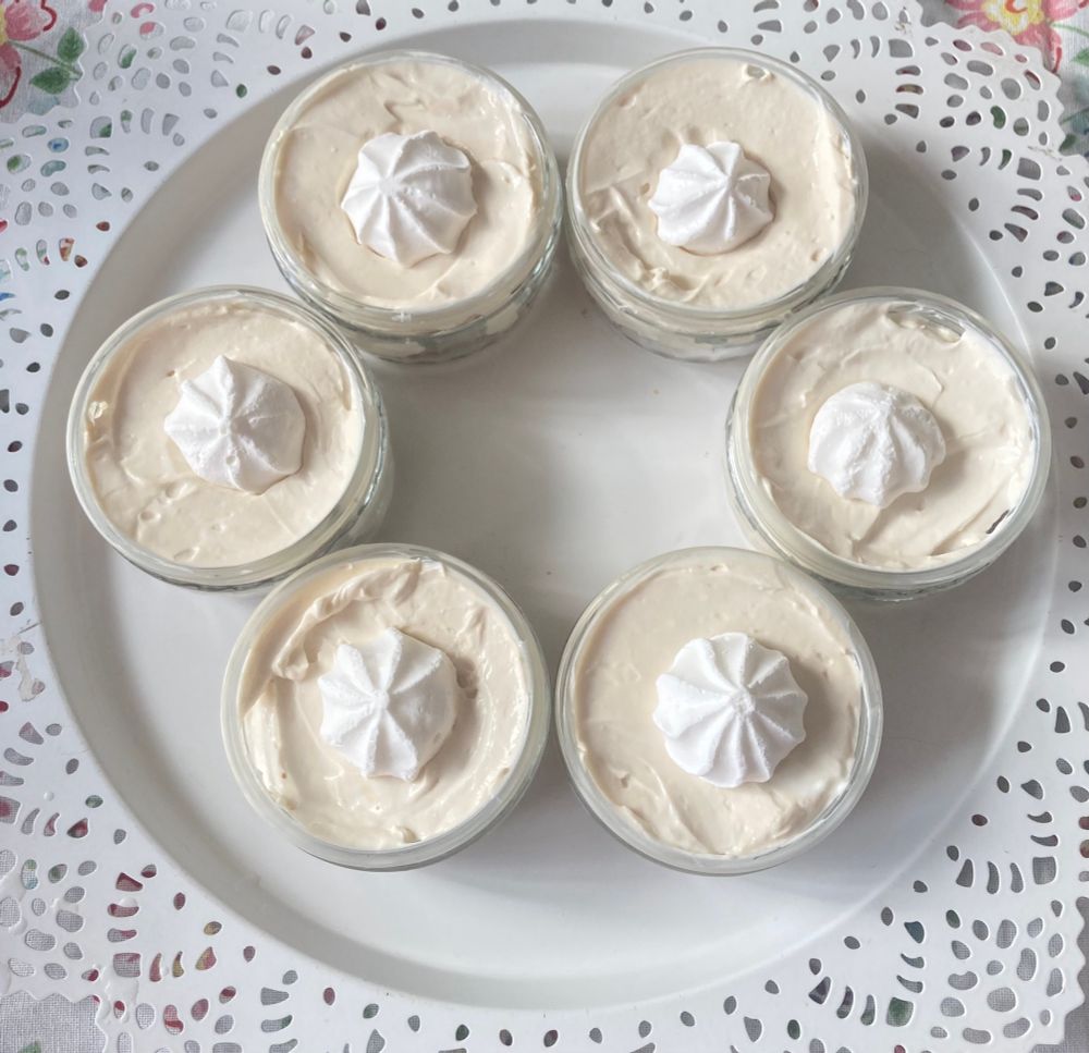 6 runde Schälchen mit weißer Käsekuchen- Creme und Baiserhäubchen auf einem runden weißen Tablett mit Lochverzierung. 