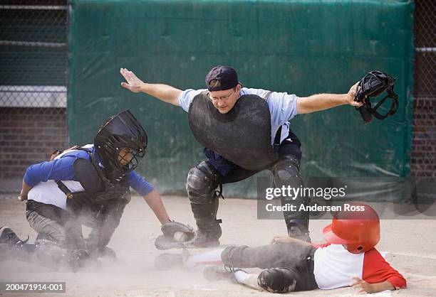 Stock pic of a baseball umpire standing over a player sliding into home, making the hand signal for “safe”