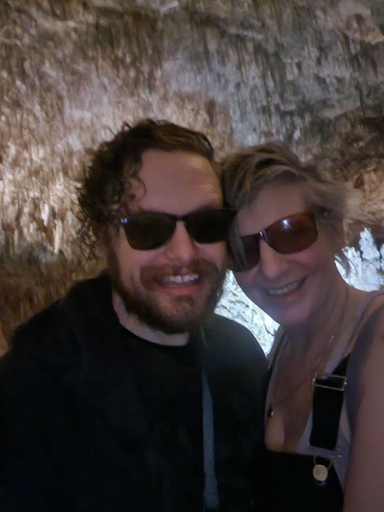 A couple in sunglasses poses in a Carlsbad Caverns, showcasing the natural landscape behind them.