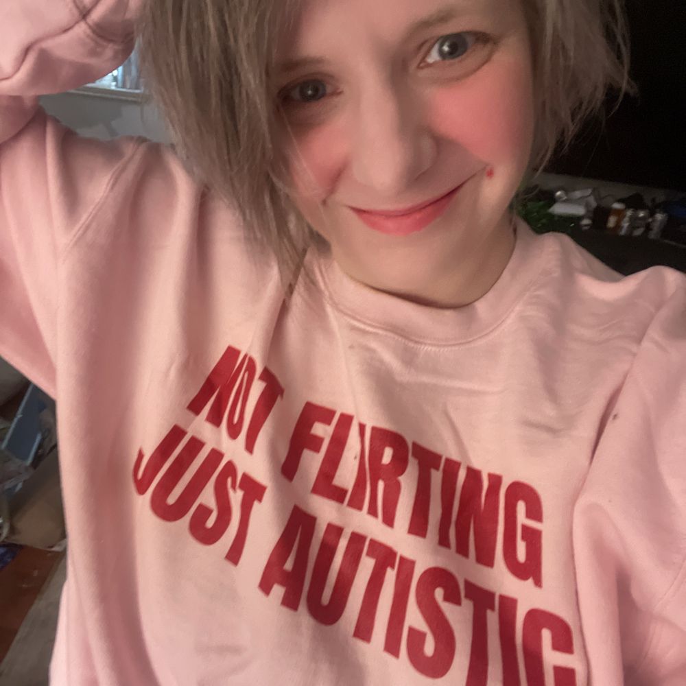 A smiling person wears a “not flirting, just autistic” shirt. 