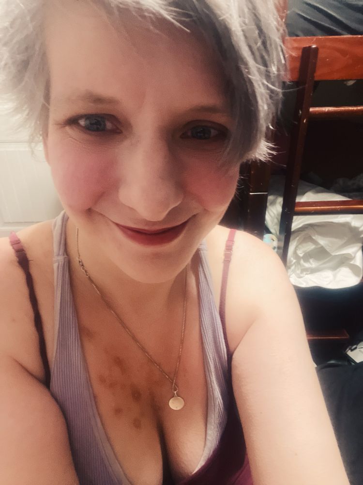 A person with grey hair wearing a necklace, smiling at the camera.