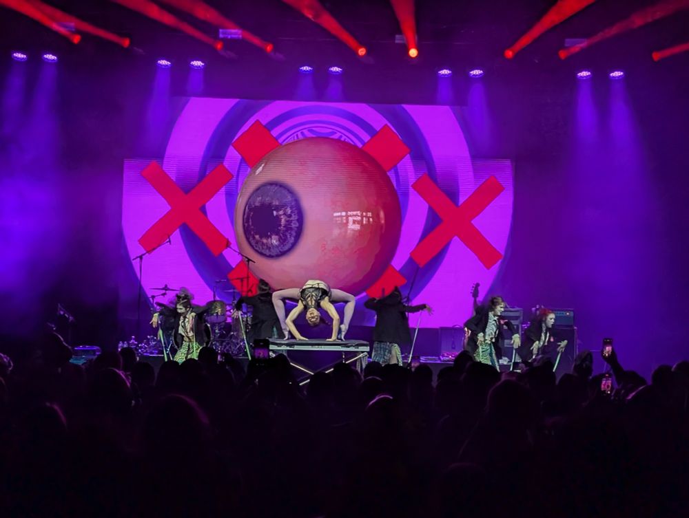 A contortionist in front of a screen with a large eye ball looking stage right.