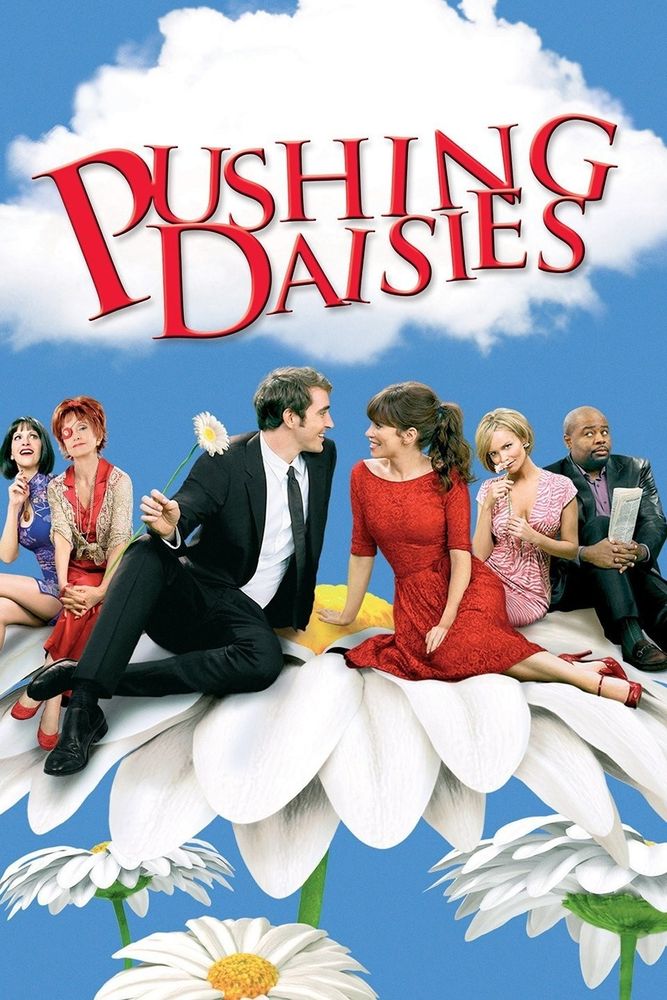 6 people sit atop a giant daisy with 3 smaller daisies underneath against a light blue background. The man on the middle left holds a daisy in his right hand while smiling at the woman to his immediate left. Above the people in red are the words "Pushing Daisies".